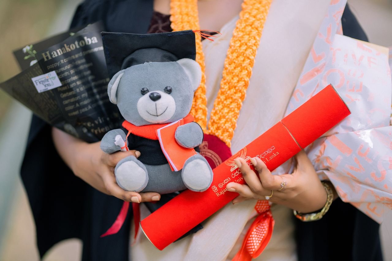Close-up of a graduate holding a cute teddy bear and diploma at a ceremony.